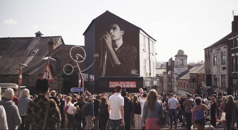 People gathered by the Ian Curtis mural in Macclesfield, linking local music heritage and community connection